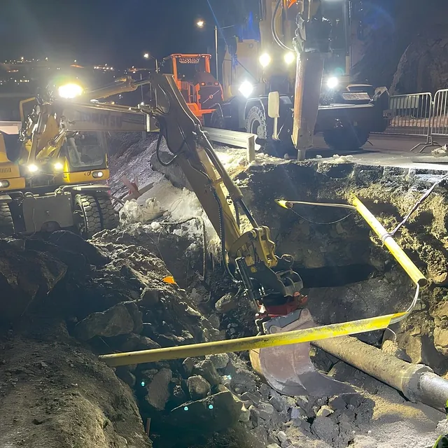 Gravearbeid om natten med gravemaskiner og store hull i bakken under kraftig lys.